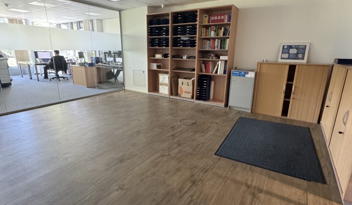 Offener Büroraum mit hellem Vinylboden, Holzregalen, niedrigen Sideboards und Blick in angrenzenden Arbeitsbereich.