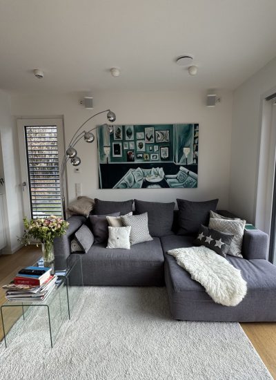 Graue Sofalandschaft unter farbenfrohem Gemälde für mehr Wohnlichkeit im lichtdurchfluteten Wohnzimmer.