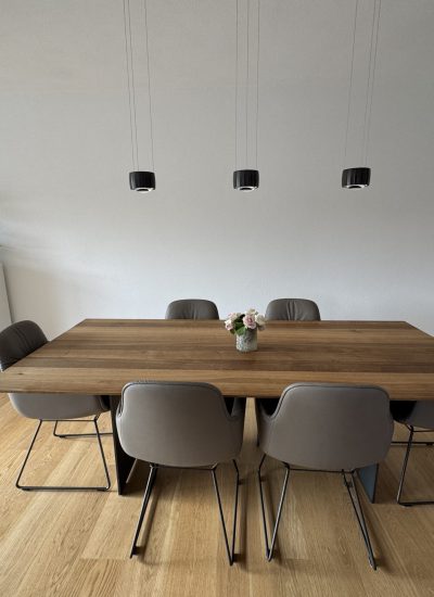 Großzügiger Esstisch aus Holz mit moderner Pendelbeleuchtung im offen gestalteten Wohnbereich des Neubaus