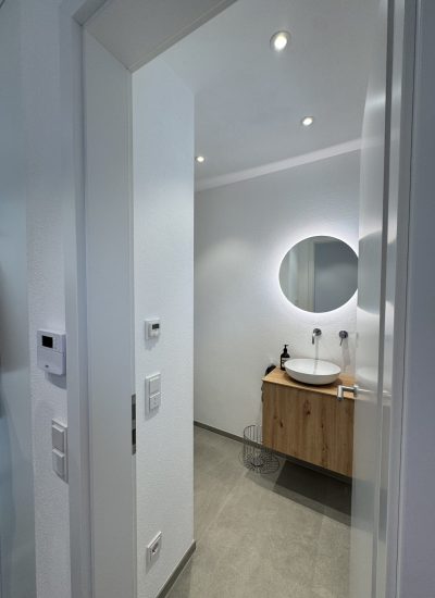 Echtholz-Waschtisch mit rundem Lichtspiegel im modernen Badezimmer passend zum neutralen Gesamtkonzept.