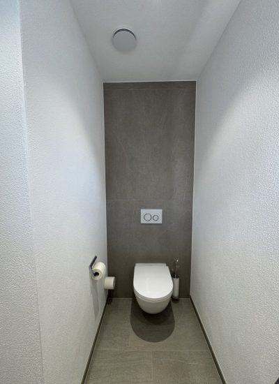 Minimalistisches Gäste-WC mit großformatigen grauen Fliesen und hochwertiger Sanitärkeramik im Neubau.