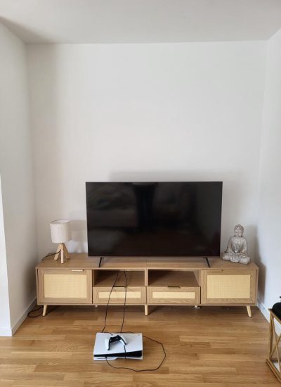 Moderner Fernseher auf hellem TV-Lowboard mit Playstation und Dekofigur.