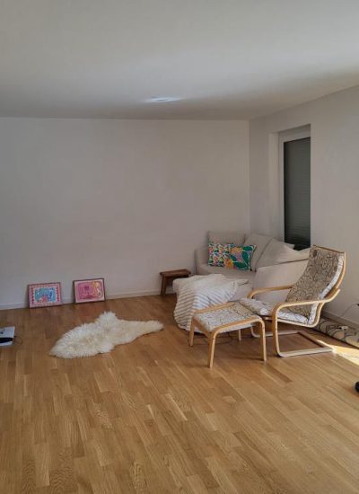 Helles Wohnzimmer mit Holzparkett, Relaxsessel, Fellteppich und goldener Stehlampe.
