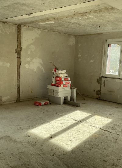 Rohbau-Innenraum mit Betonwänden, zwei Fenstern in Renovierungszustand.